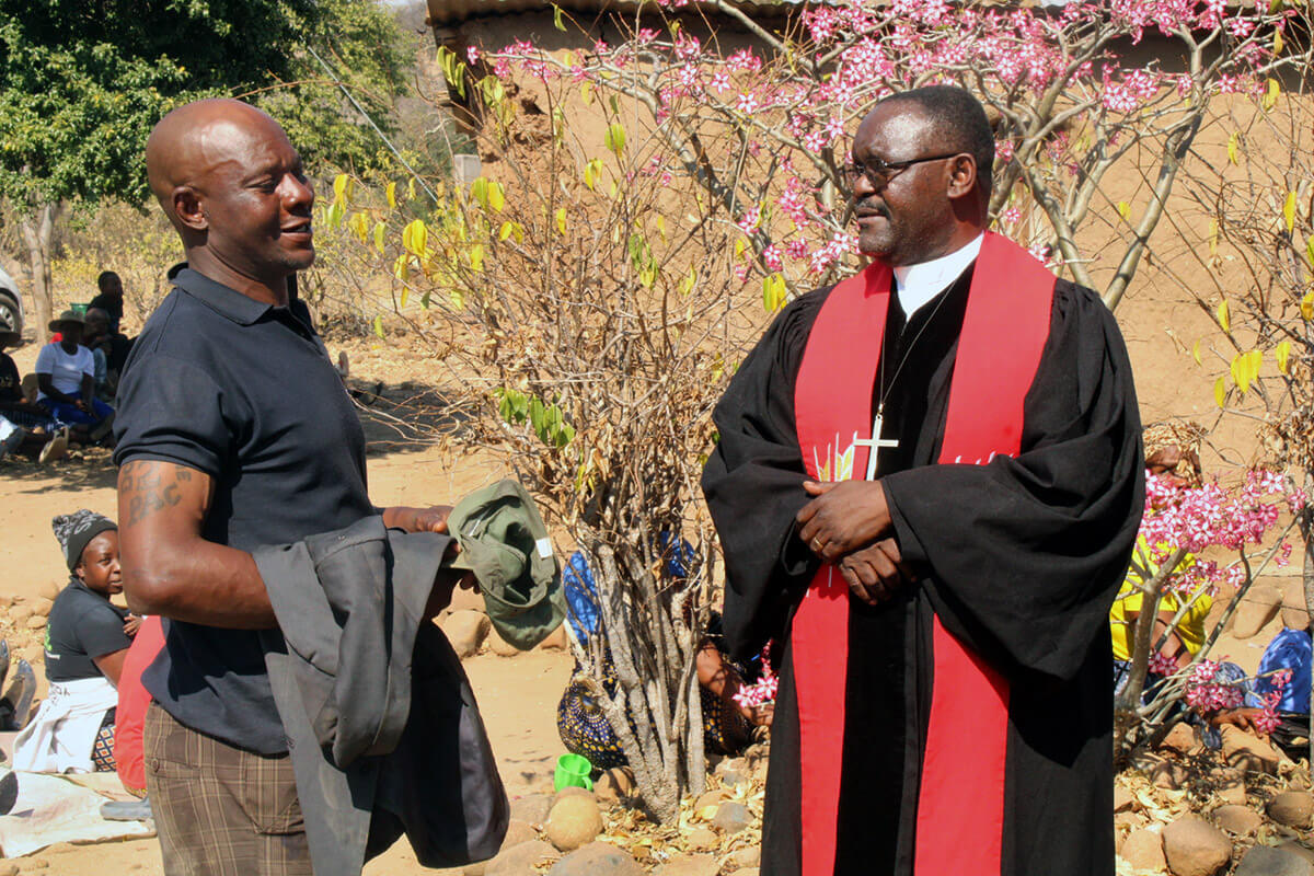 Danny Dube (à gauche), membre régulier de Morning Service à Nyanyadzi, Zimbabwe, s'entretient avec le révérend Godfrey Gaga, pasteur responsable du circuit de Nyanyadzi, après un enterrement. Le service religieux de 7 heures du matin a transformé Dube, qui était connu dans la communauté pour sa consommation d'alcool et ses troubles. "Le circuit rencontre les gens là où ils sont, offre un espace sûr pour la transformation et montre que l'église est un lieu de guérison plutôt que de jugement", déclare l'évêque Gift K. Machinga. Photo par Kudzai Chingwe, UM News. 